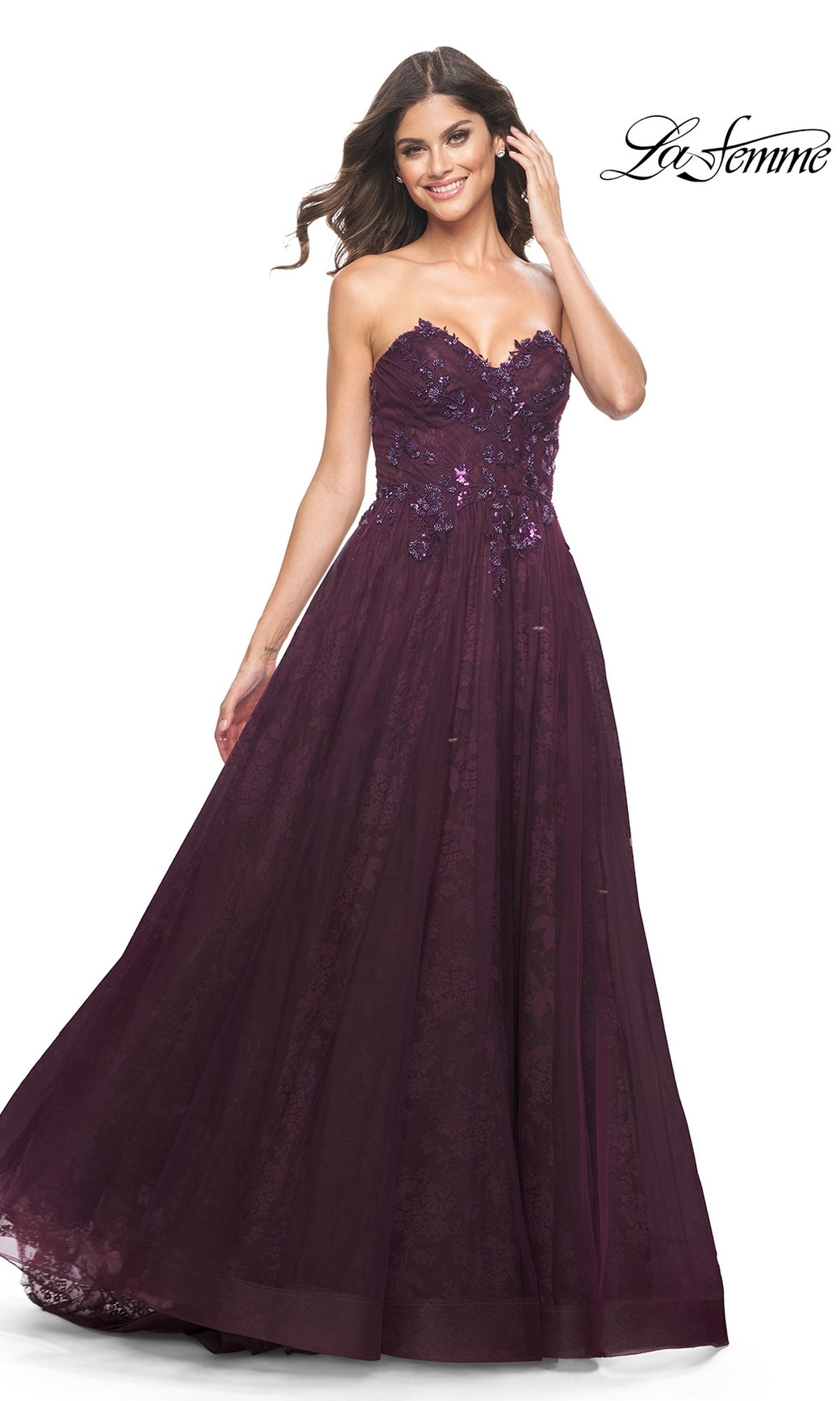 A woman models the La Femme Strapless Long Prom Ball Gown 31954, a floor-length dark purple dress with a sweetheart neckline and lace floral appliqué, standing against a white background.